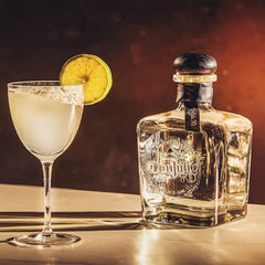 Don Julio tequila bottle with a cocktail garnished with a lime wheel on a wooden surface.