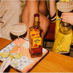 Bottle of Jose Cuervo El Dorado tequila with two cocktails on a table.