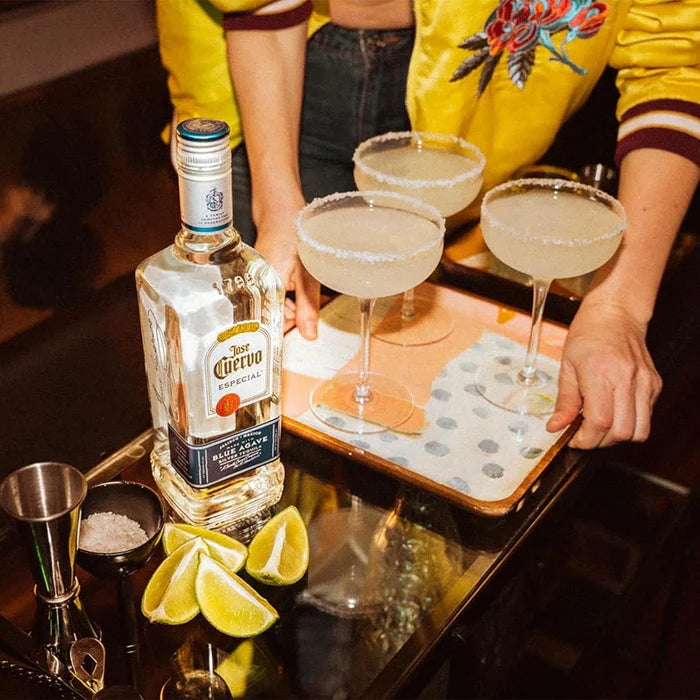 Person holding a bottle of Jose Cuervo with three margaritas on a tray.