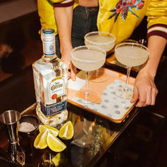 Person holding a bottle of Jose Cuervo with three margaritas on a tray.
