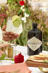 Hendrick's gin bottle with a cocktail and snacks on a table outdoors.