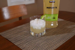 Glass of margarita with lime wedge next to a bottle of Kirkland margarita on a textured surface.