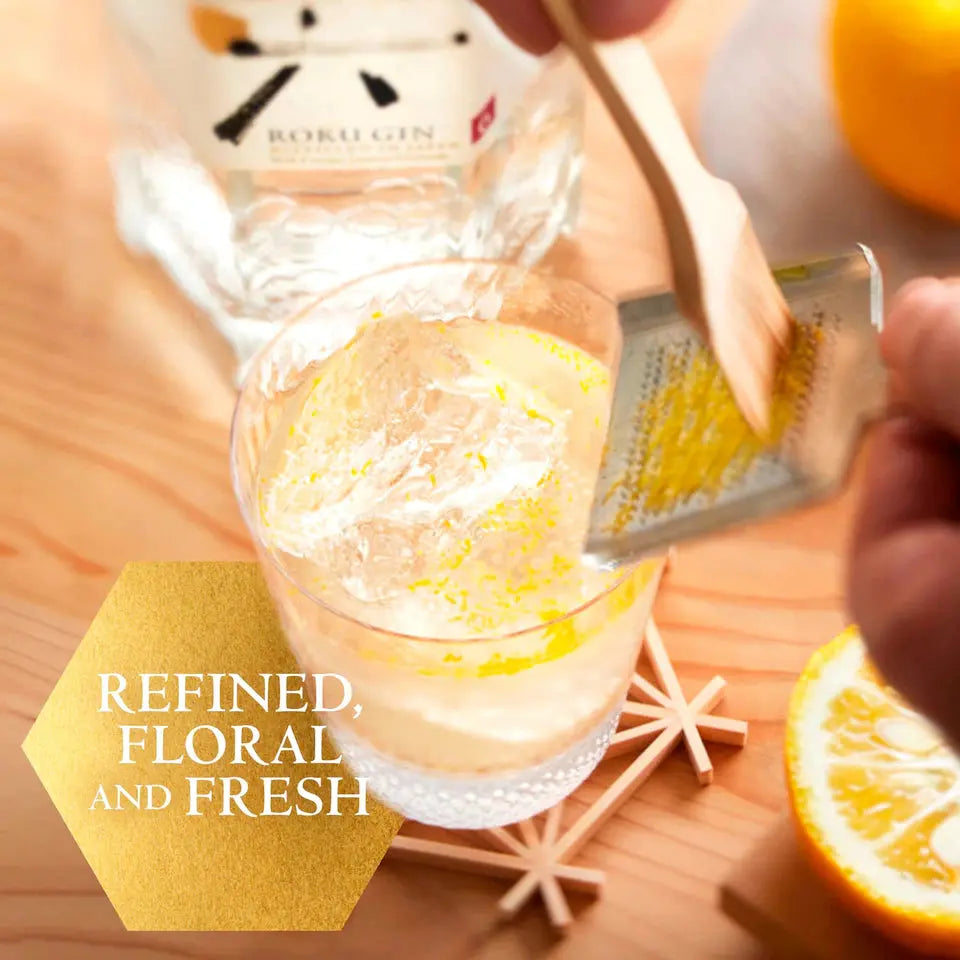 Glass of gin with lemon zest, grater, and bottle labeled 'Bokul Gin' on a wooden surface.