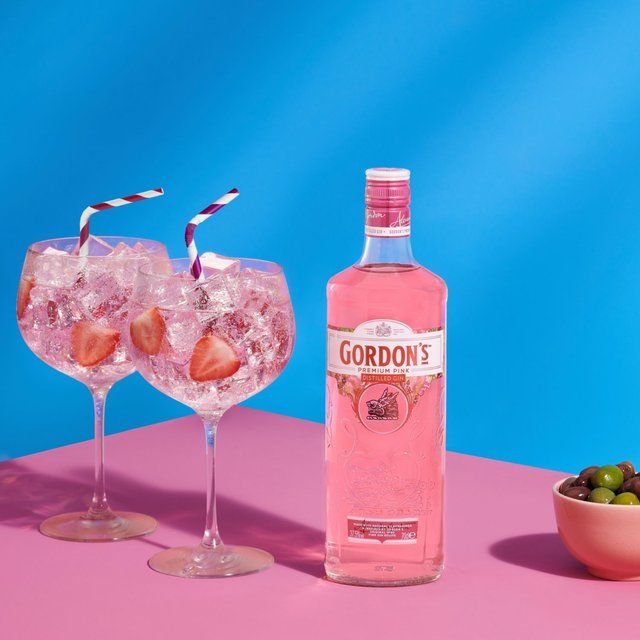 Pink gin bottle with two glasses of pink cocktail and a bowl of olives on a blue and pink background