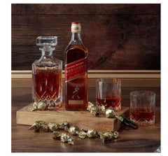 Johnnie Walker Red Label whisky bottle with decanter and glasses on a wooden surface.