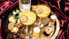 Two cocktails with passion fruit garnishes on a gold tray with an Absolut Vanilla bottle, surrounded by red fabric.