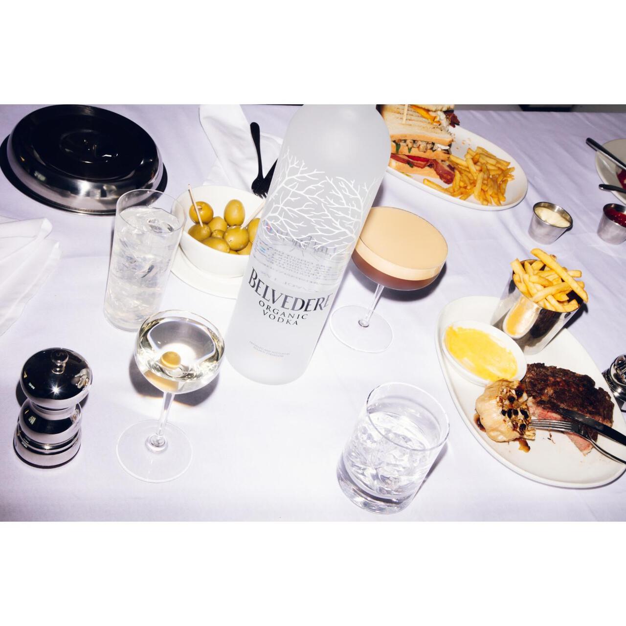 Dining table with food and drinks, including a bottle labeled 'Briyeder' and a steak dish.