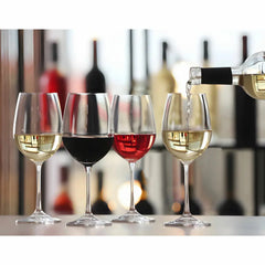 Four wine glasses with different colored wines being poured, with blurred bottles in the background.