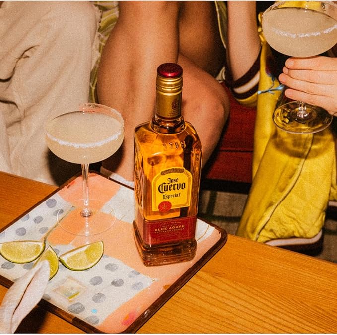 Bottle of Jose Cuervo El Dorado tequila with two cocktails on a table.