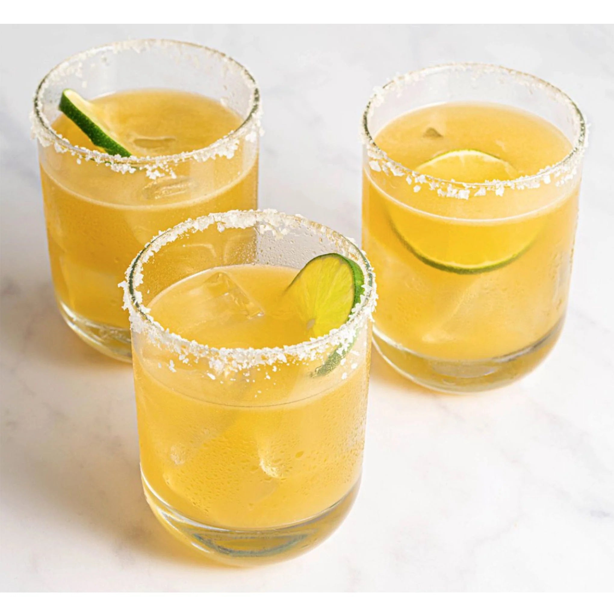 Three glasses of yellow cocktails with lime wedges on a white background