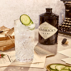 Hendrick's Gin bottle with a cocktail garnished with cucumber on a textured surface.