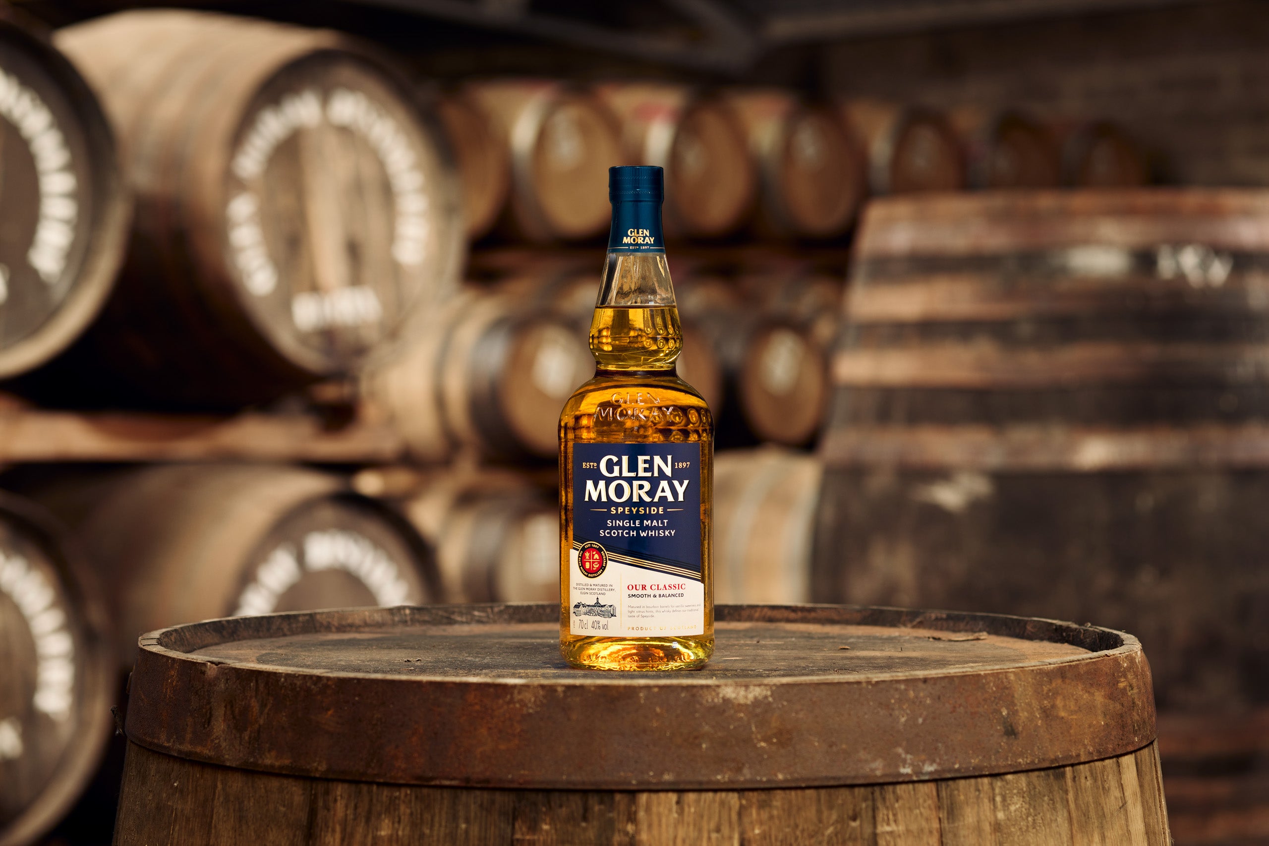 Glen Moray whisky bottle on a wooden barrel with barrels in the background
