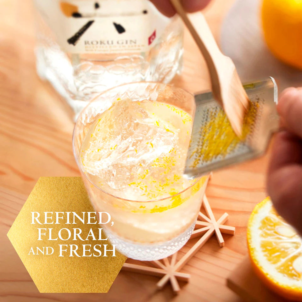 Glass of gin with lemon zest, grater, and bottle labeled 'Bokul Gin' on a wooden surface.