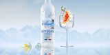 Grey Goose vodka bottle with a glass of vodka and orange slice against a mountainous background